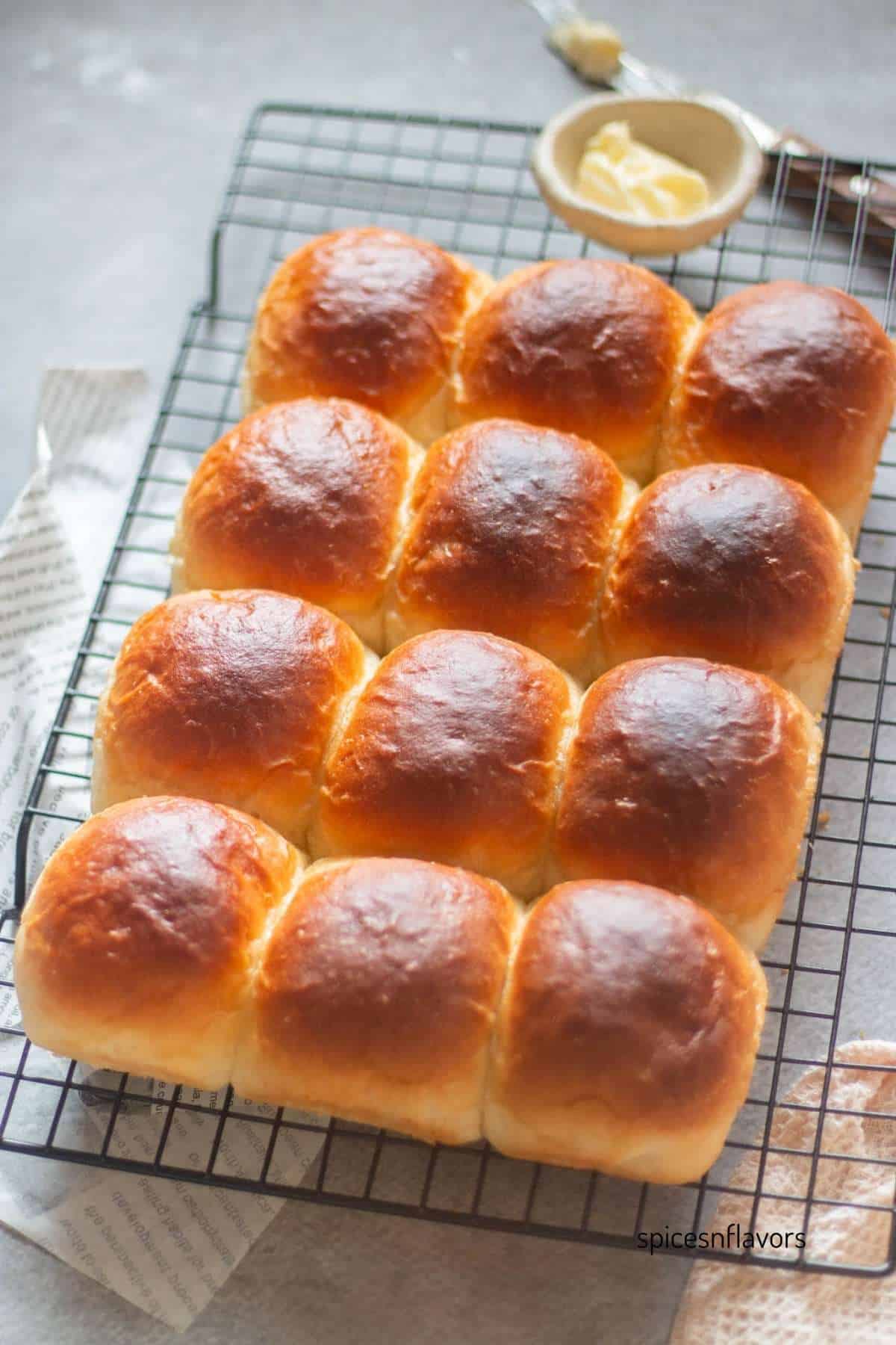 baked dinner rolls placed on a wire rack with butter bowl and knife on the side