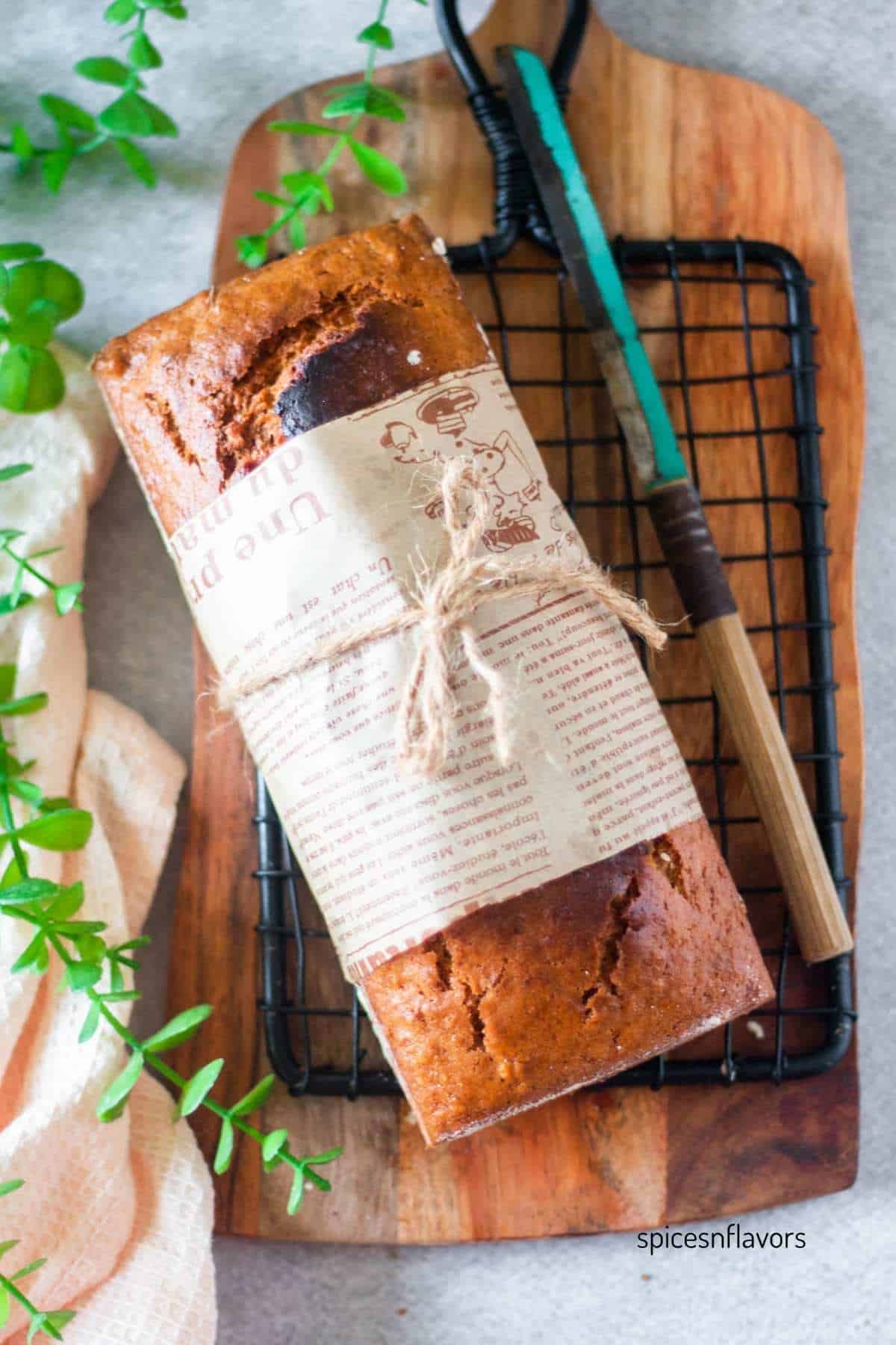 loaf of banana bread with mayo on wire rack with knife on side
