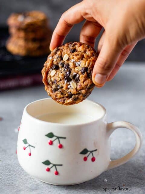 one oatmeal chocolate chip cookie held in hand ready to be dipped in milk