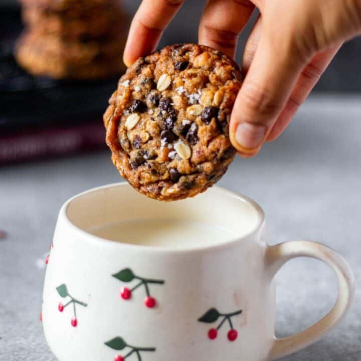 one oatmeal chocolate chip cookie held in hand ready to be dipped in milk