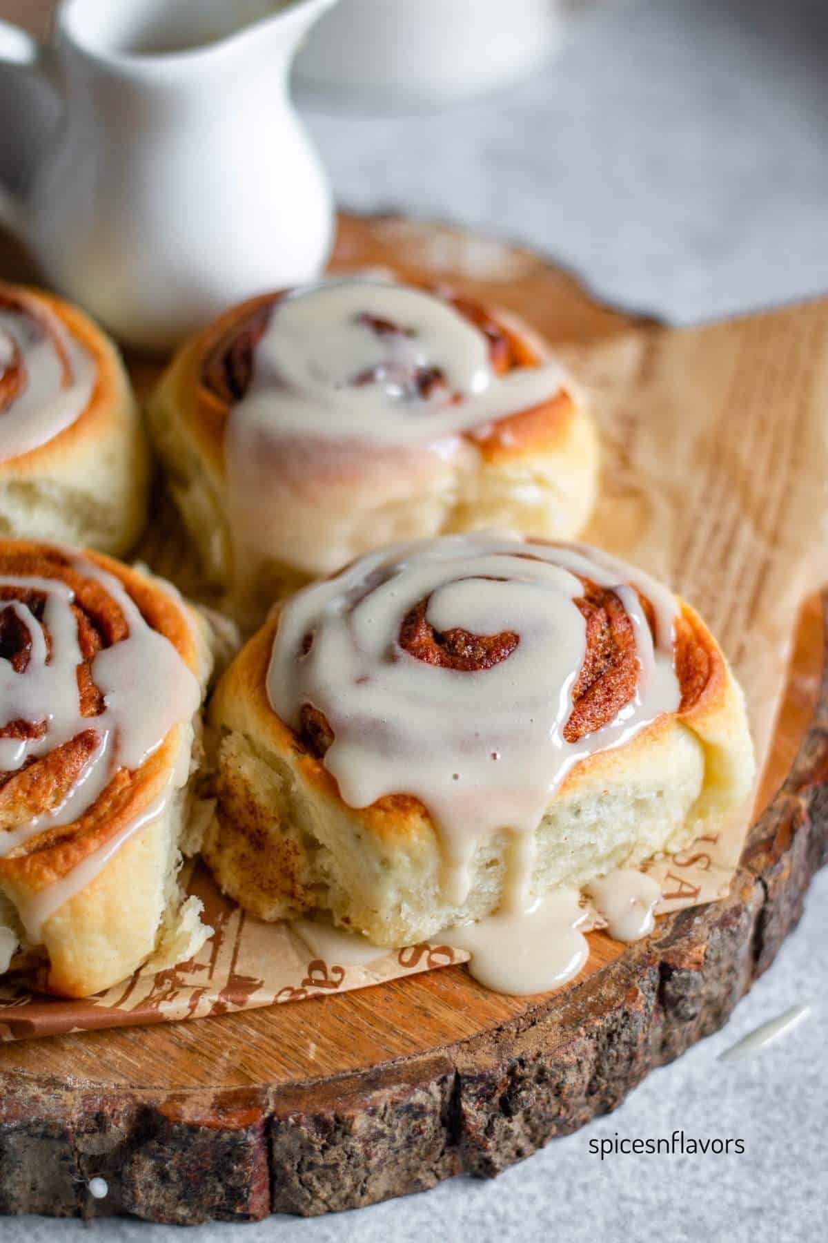 4 pieces of cinnamon rolls with frosting placed on a wooden chopping board