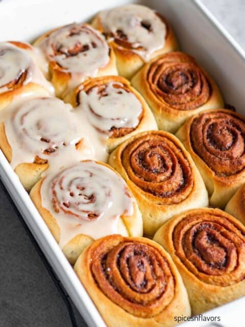 baking pan with baked cinnamon rolls and half of it frosted with glaze