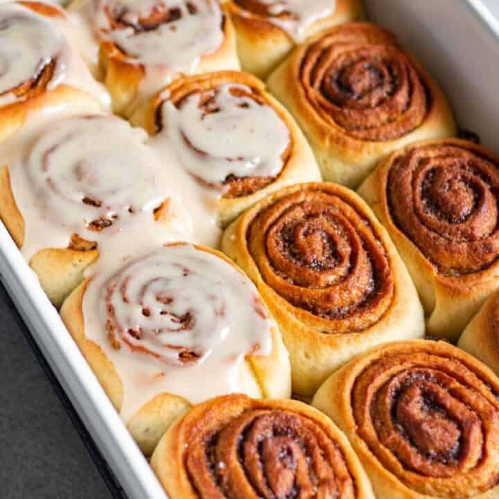 baking pan with baked cinnamon rolls and half of it frosted with glaze
