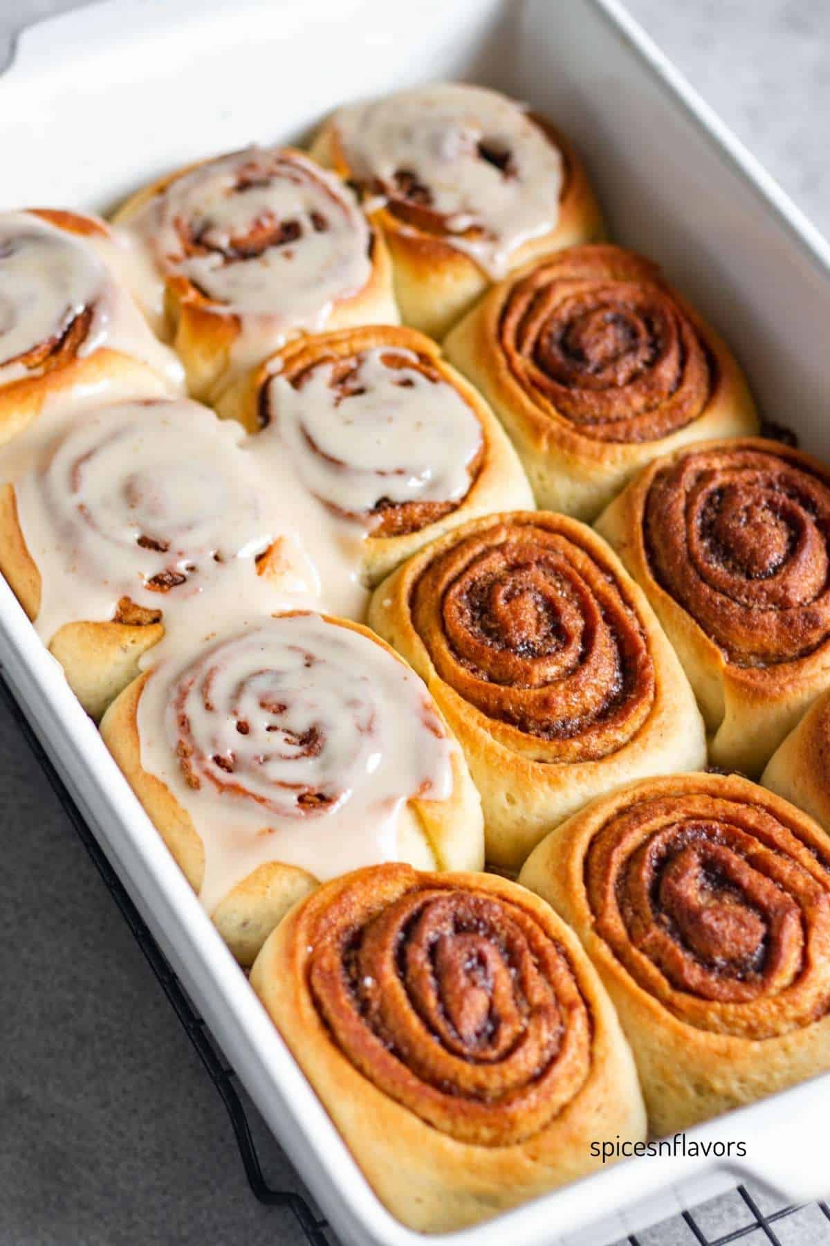 baking pan with baked cinnamon rolls and half of it frosted with glaze