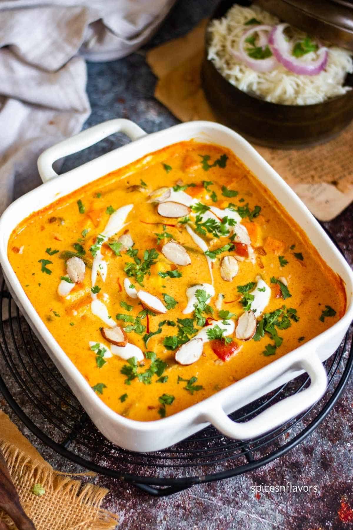 mixed vegetable paneer curry served in a casserole garnished with almonds and cream