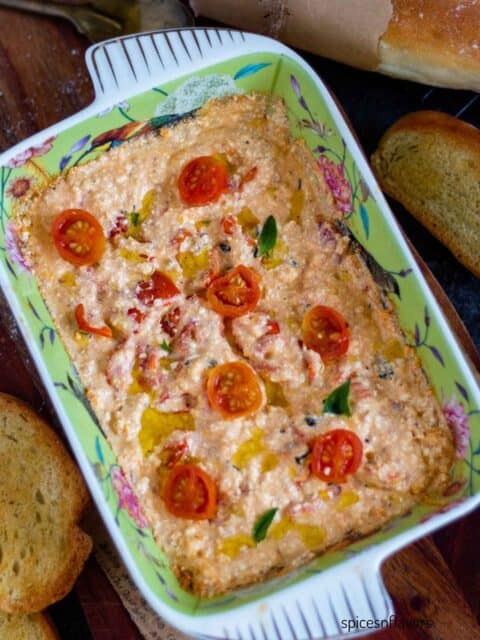 baked feta dip served in casserole with cherry tomatoes on top