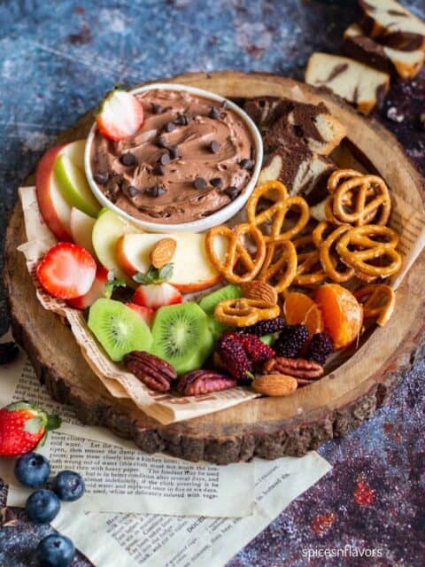 brownie batter dip in white bowl with fruits and pretzels around it