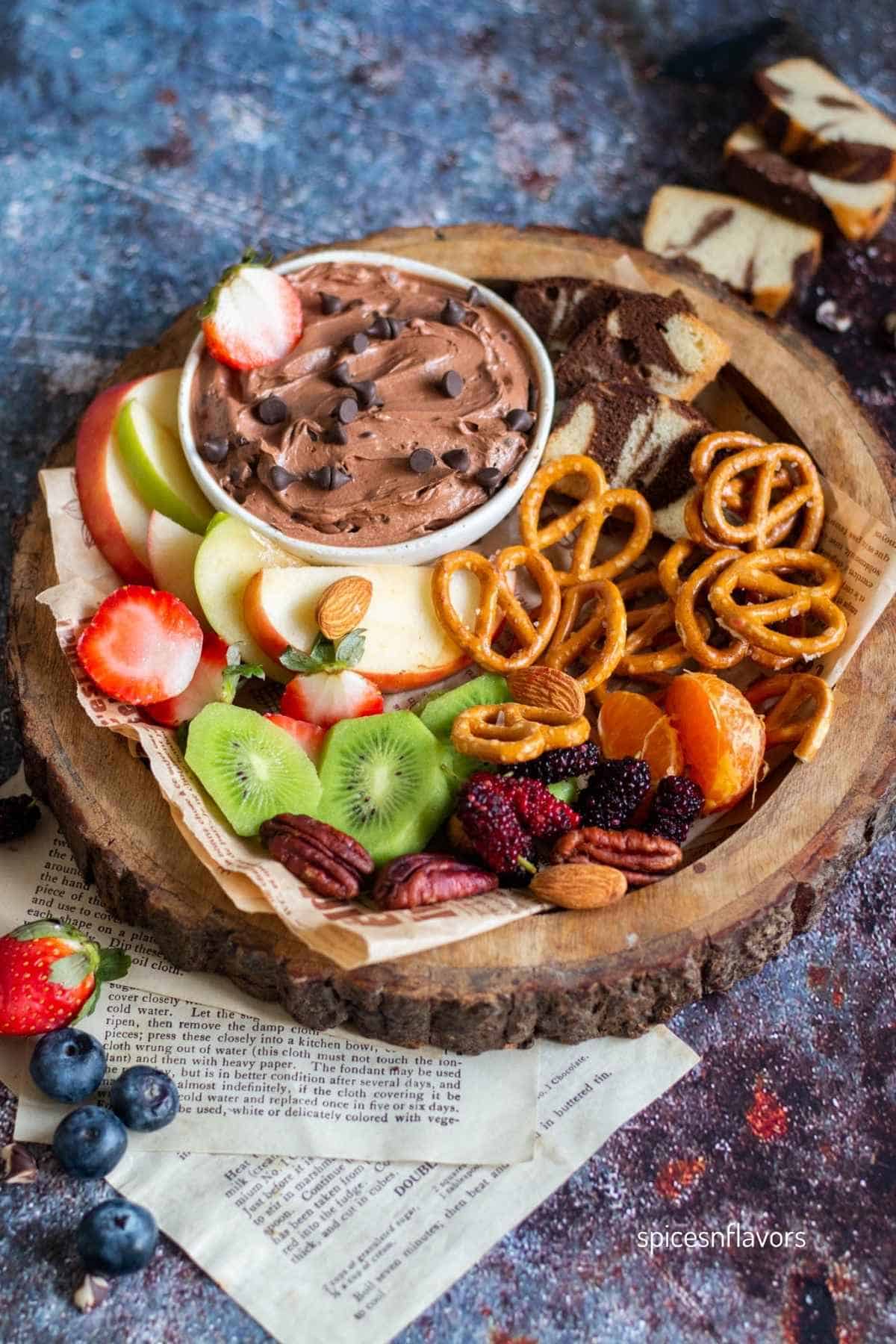brownie batter dip in white bowl with fruits and pretzels around it