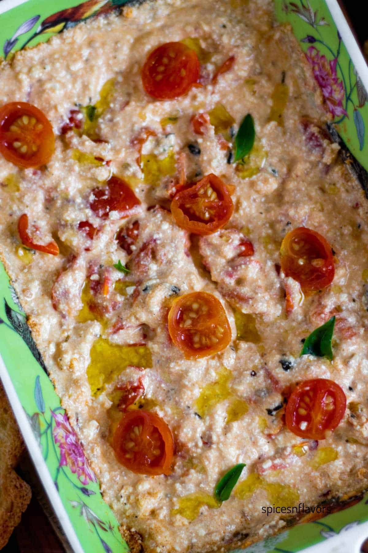 mashed up baked feta cheese with oil and halved cherry tomatoes on top