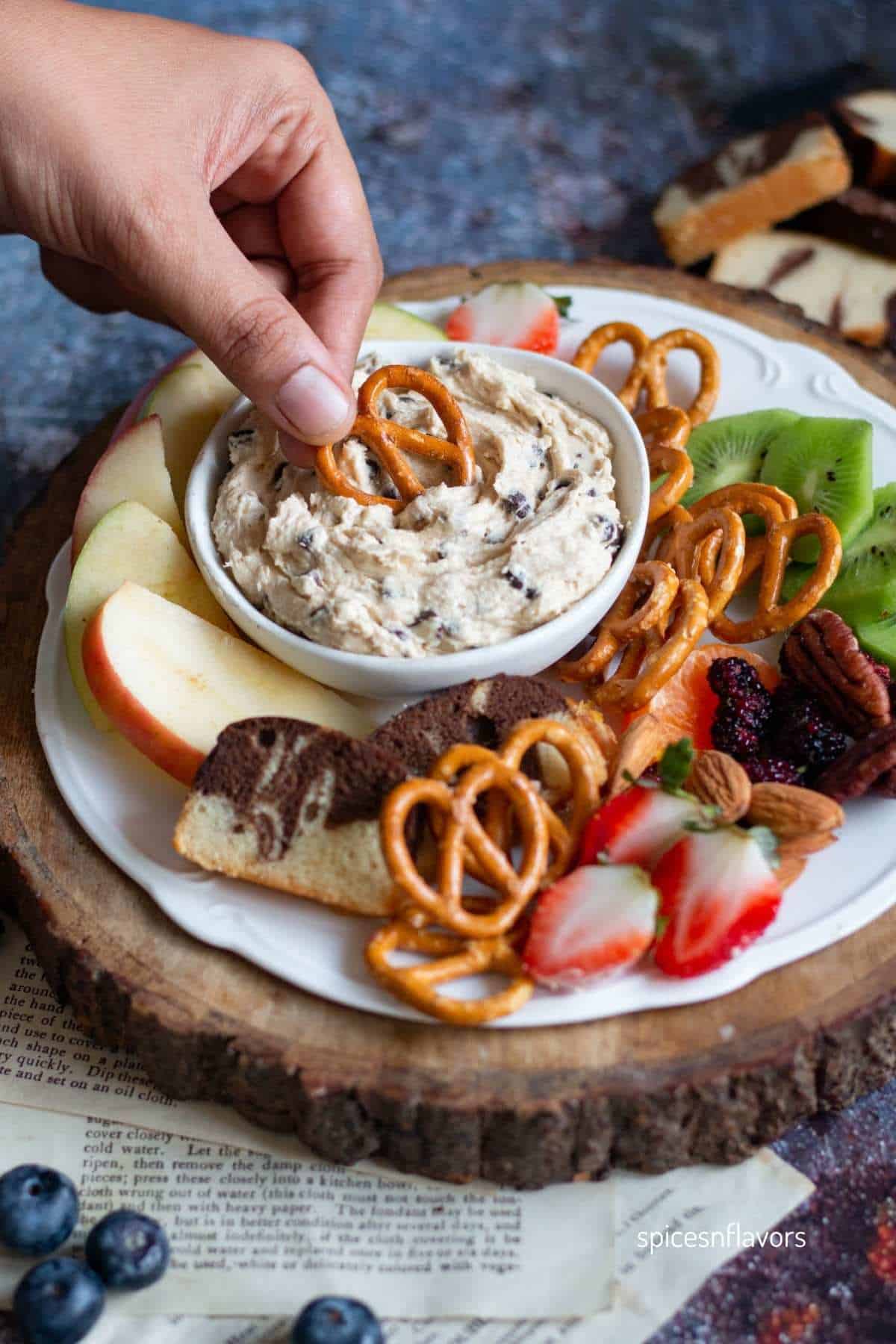 dipping pretzel in chocolate chip dip placed in a bowl over white plate