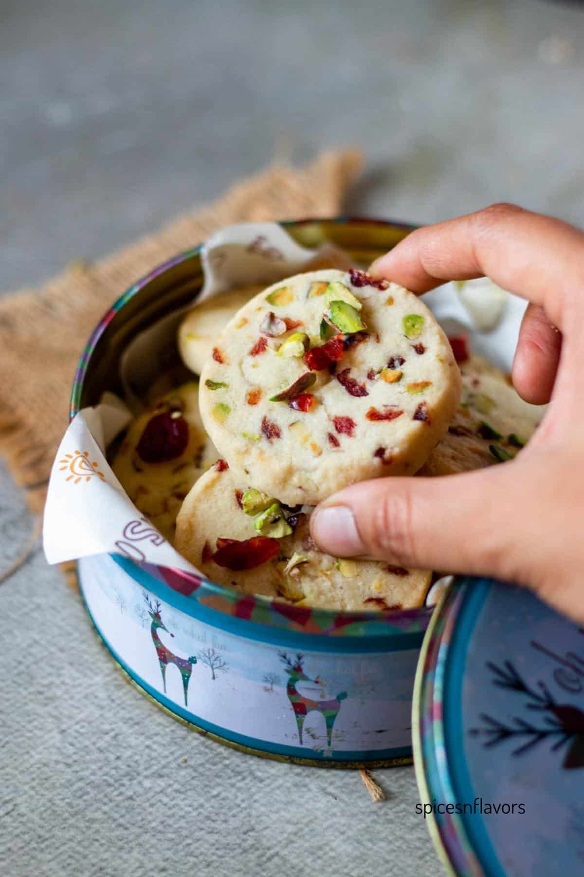 picking up cranberry pistachios shortbread cookies from cookie tin