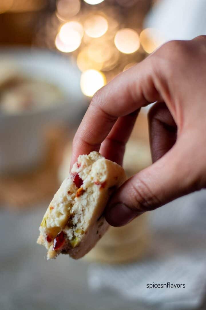 sliced cranberry pistachio shortbread cookies held in your fingers