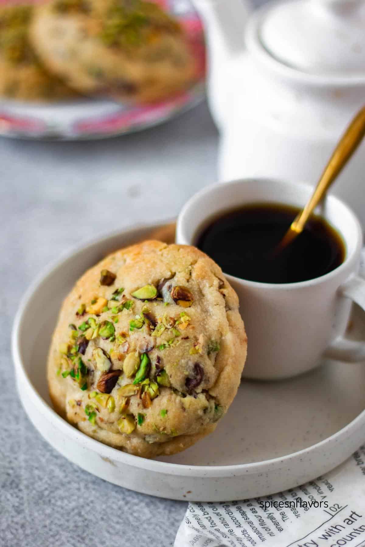 one piece of triple chocolate pistachio stuffed cookie placed in a plate with a coffee cup behind it
