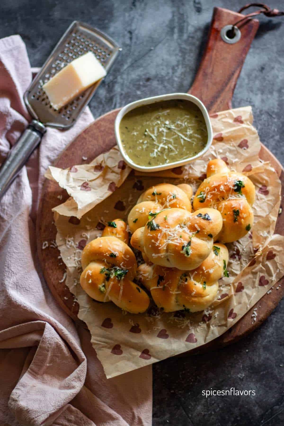 baked garlic knots placed on wooden board with cheese and pesto on side