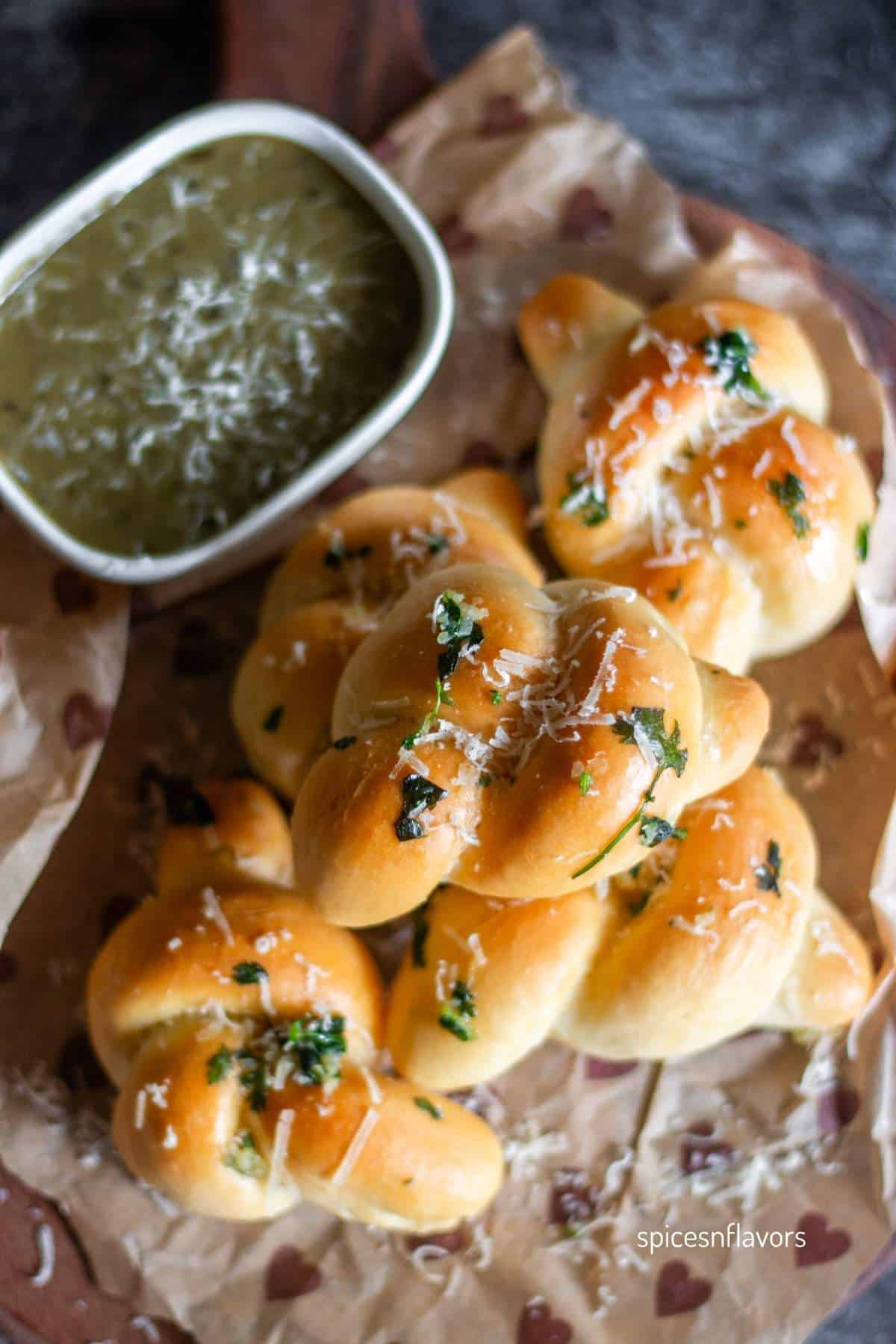 baked garlic knots stacked on top of each other with pesto on the side.
